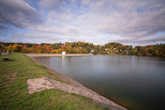 View of Velka Richnava lake with autumn foliage on the surrounding hills and a stone embankment in Stiavnicke Bane, Banska Bystrica Regio, Slovakia.
