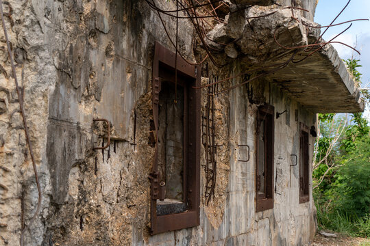 View of the ruins of the North Field Base, featuring weathered concrete walls, exposed rusted rebar, and empty window frames in Northern Tinian, Tinian, Northern Mariana Islands.