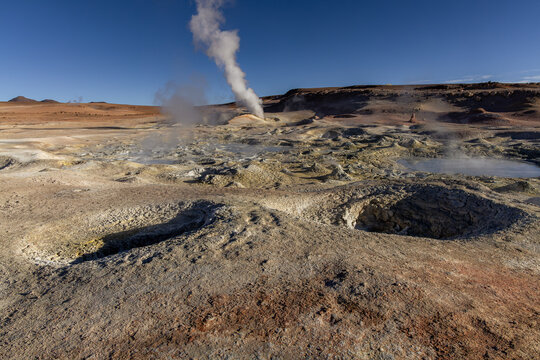 View of Geisers Sol de la Manana with geothermal steam vents, bubbling mud pools, and volcanic terrain under a clear blue sky in Sur Lipez, Potosi Department, Bolivia.
