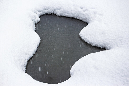 Fresh white snow surrounds a dark, open patch of river water during a mild March thaw, capturing the beautiful transition from winter to spring in a quiet natural scene