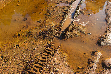Naklejka premium Deep tire tracks from an enduro motorcycle carved into the wet sandy soil of a quarry with muddy puddles, showcasing intense off-road adventure and challenging riding conditions
