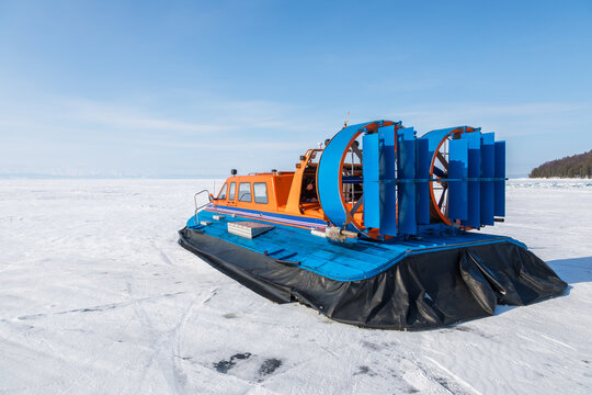 View of an orange and blue hovercraft resting on the vast frozen surface of Lake Baikal under a clear blue sky in Severobaykalsk, Buryatia, Russia.