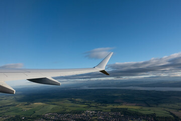 Fototapeta premium A scenic airplane window view showing the aircraft wing flying over the green fields, towns, and the Firth of Forth bay in Scotland