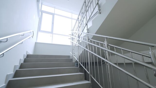 Wide staircase leads toward bright window in modern building. High quality metal handrails ensure safety and comfort for all visitors
