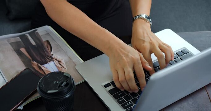 Hands working on laptop keyboard for administrative correspondence, envelope and magazine on table, coffee cup and watch visible calm productive scene of schedule management and client email handling.