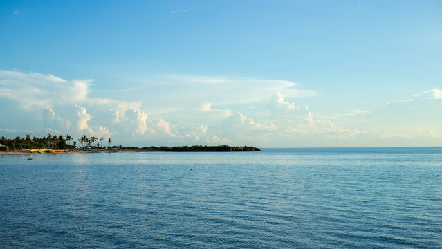 View of Bantayan Island with palm trees along the sandy coastline, calm blue sea, and fluffy white clouds in the sky in Cebu, Central Visayas, Philippines.