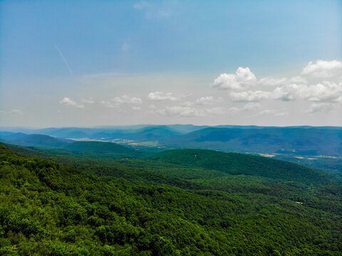 Lost City, West Virginia, United States - 12 June 2019: Aerial view of the lush green Appalachian Mountains, featuring dense forest canopy under a bright blue sky with scattered clouds.