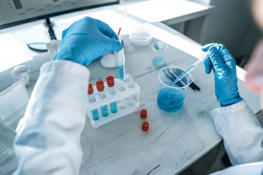 Close up of a researcher performing chemical analysis with blue solutions in a bright laboratory setting. Laboratory tools and digital technology highlight innovation in scientific research