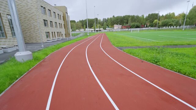 Running track with white markings curves between green grass lawns. Professional rubber surface provides ideal conditions for morning jog