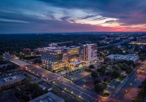 Reston, Virginia, United States - 27 May 2020: Aerial view of modern office buildings and residential complexes illuminated at dusk under a vibrant sunset sky.
