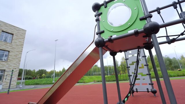 Complex climbing structure with ropes and slides stands on playground. Educational facility enveloped with trees creates quiet backdrop