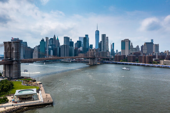 New York, United States - 11 August 2021: Aerial view of the Brooklyn Bridge spanning the East River with the Manhattan skyline, skyscrapers, and Jane's Carousel under a blue sky.