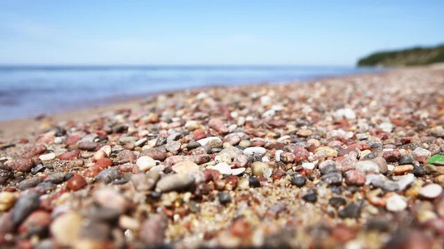 Colorful pebble covered shoreline under clear sky beside calm sea with distant green landscape