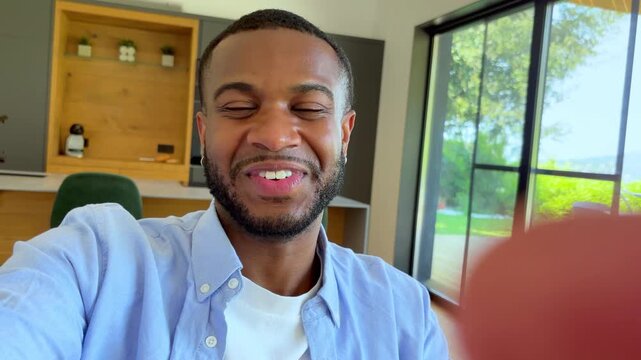 A handsome young Black man with a beard smiles broadly and nods at the camera, exuding happiness and positive vibes. He appears cheerful and friendly, possibly during a video call or a casual conversa