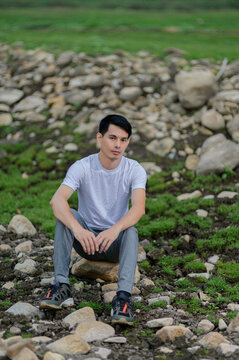 Young man sitting on rocky terrain with greenery and stones in the background