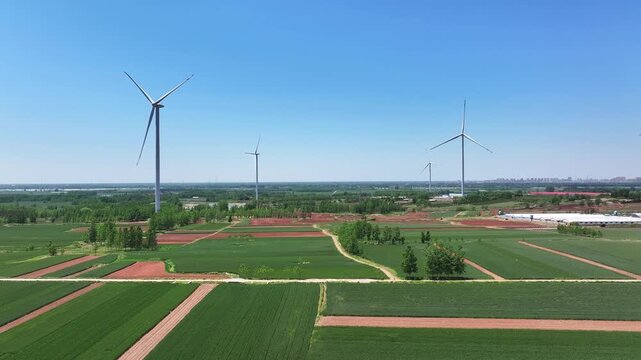 Multiple wind turbines standing tall across green and red agricultural fields under a clear blue sky