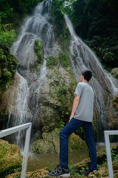 Young Man Enjoying Scenic View of Waterfall in Forest Nature Spot