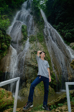 Young woman standing at waterfall with lush greenery and rocks in scenic nature landscape