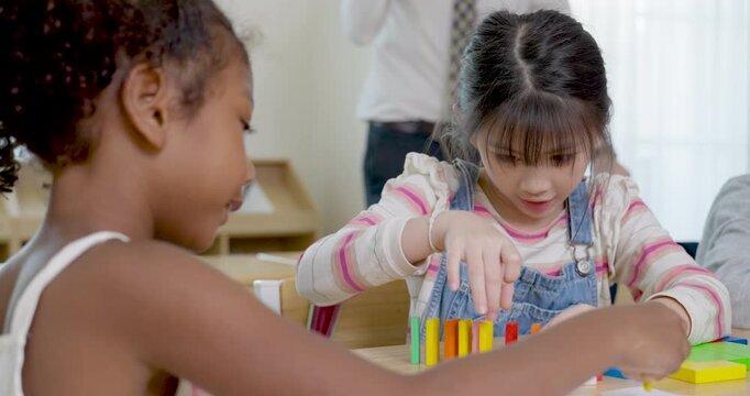 Two elementary girls arrange colorful blocks at wooden desk during back to school group activity, peer communication builds teamwork, pattern thinking, confidence, cooperation, classroom readiness