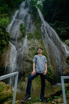 Young man standing in front of a majestic waterfall surrounded by lush greenery