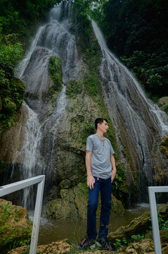 Young man admiring cascading waterfall in lush green jungle setting