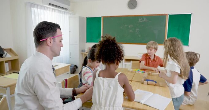 Wide classroom scene with adult male teacher guiding multicultural pupil group during block activity at desks, building teamwork, peer discussion, motivation, and back to school engagement today.