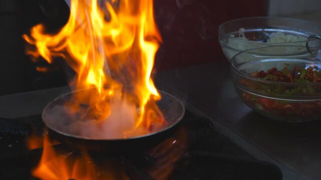 Unrecognizable chef cooking flambe style dishfrying vegetables on pan in modern kitchen of restaurant. Close up of flaming skillet on gas plate. Meal preparation concept. Slow motion