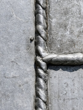 Weld seam on metal sheet, top down industrial detail, gray aluminum panel with clean shadow and tiny weld spatter
