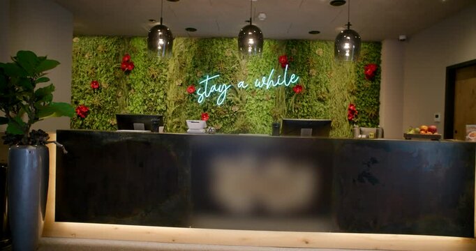 Empty hotel front desk area with illuminated neon sign on decorative green plant background
