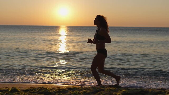 A fit woman runs on the shoreline during a beautiful sunrise, embracing a healthy lifestyle and outdoor fitness. The tranquil ocean and warm sunlight create a serene, inspiring atmosphere