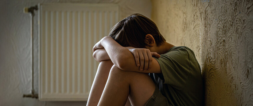 Bullying. Lonely boy sits in room. Scared fearful small boy covering face. Sad child suffering from depression sitting alone in home loneliness