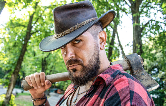 Lumberjack with plaid shirt among the trees. Lumberjack man. Bearded cowboy lumberjack with a large ax