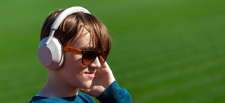 Sunglasses, headphones. Teenage boy with headphones listening to music on a mobile, nature, outdoor, green, grass, outside