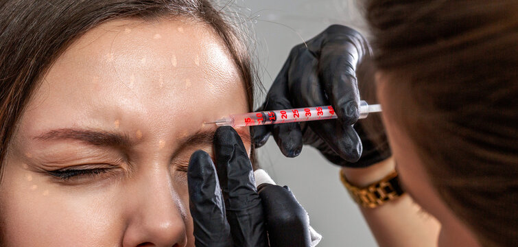 Filler injection in forehead. Woman receiving injection of anti-aging botox filler to forehead from cosmetologist. Beautician expert's hands injecting botox in female forehead