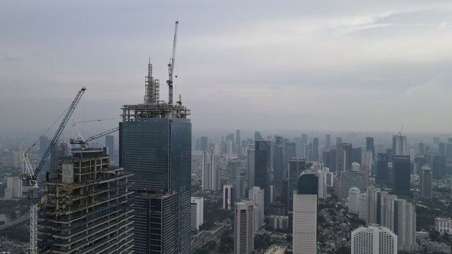 Kecamatan Menteng, Indonesia - 03 December 2021: Aerial view of skyscrapers under construction with tower cranes in Jakarta Pusat, set against a cloudy sky over the urban sprawl.