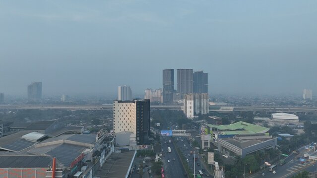 Bekasi Barat, West Java, Indonesia - 20 June 2026: Aerial view of the urban landscape featuring modern high-rise buildings, a busy highway, and dense infrastructure under a hazy sky.