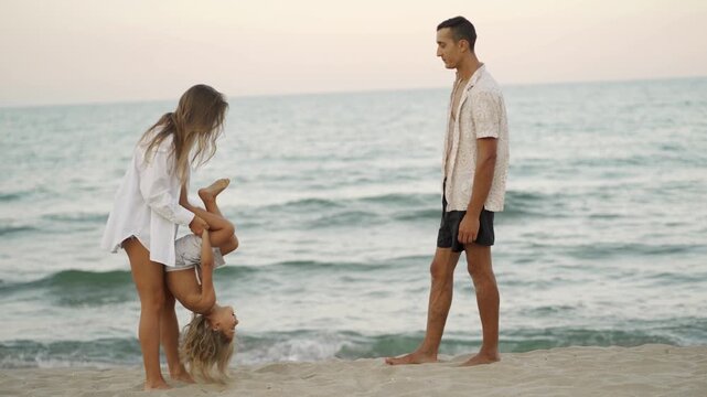 Mother and child play joyfully on the beach while father watches, all surrounded by the serene ocean at dusk. Warm light and relaxed atmosphere highlight family love and summer fun