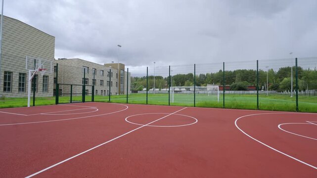 Professional sports ground features rubber surface near school. Overcast sky and lush greenery add calm atmosphere to urban athletic zone