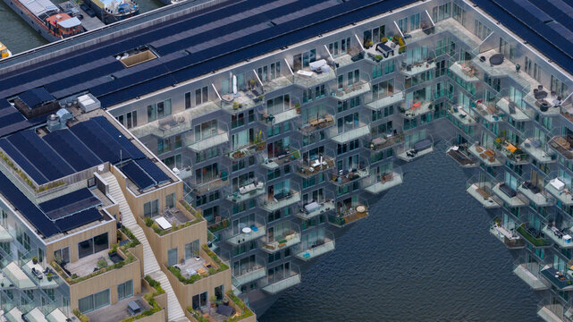 Amsterdam, Netherlands - 07 June 2026: Aerial view of Sluishuis, a modern residential building with a unique cantilevered design, balconies, rooftop terraces, and solar panels on the water.