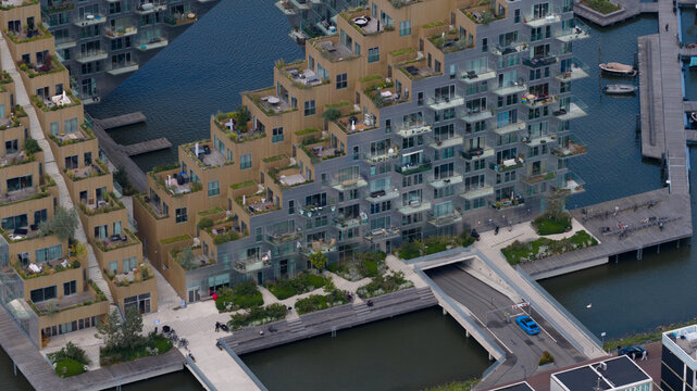 Amsterdam, Netherlands - 07 June 2026: Aerial view of the Sluishuis building, featuring its angular architecture, terraced balconies with greenery, and a water-level entrance with a blue car.