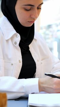 Arab Woman Sketching Designs And Writing Notes At Bright Workspace, Black Hijab And White Jacket, Concentrated