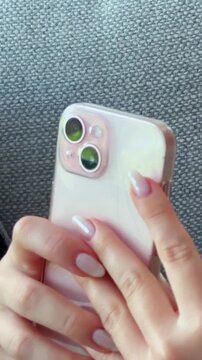 A close-up shot of hands holding a modern smartphone with a clear case and visible camera lenses. The person's manicured fingers are poised to interact with the mobile device, highlighting digital con
