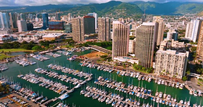 Ala Wai boat harbor with Honolulu skyline and Ko'olau mountains, Hawaii. Crowded marina, tall residential tower, lush green mountain range backdrop and partly cloudy sky in warm morning light.