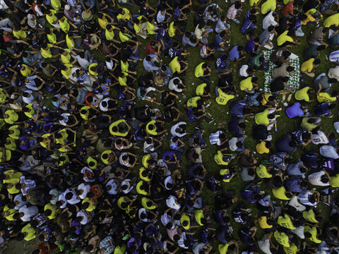Dhaka, Bangladesh - 20 June 2026: Aerial view of a large crowd of people gathered on a grassy field, wearing colorful jerseys and sitting together.