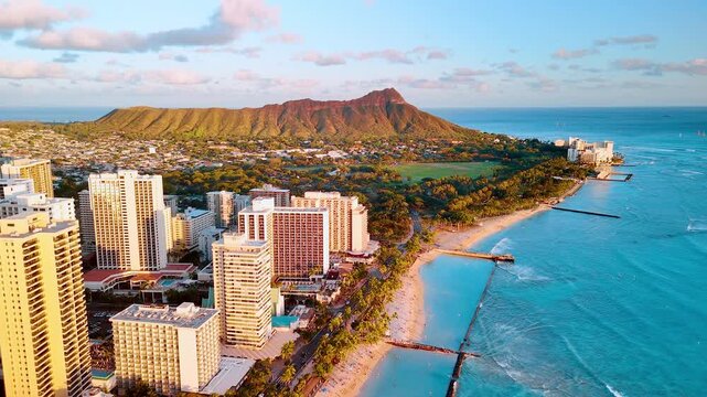Waikiki beach hotels and Diamond Head from elevated oceanside angle, Hawaii. Hotel tower row beside sandy shore, rocky breakwater pier, turquoise water, volcanic crater and open ocean at golden hour.