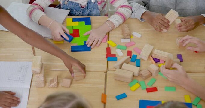 Top view of elementary pupil group sorting colorful blocks on wooden desk with notebooks nearby, back to school hands on math activity builds teamwork, pattern thinking, participation, confidence
