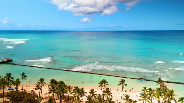 Waikiki beach waterfront with palm tree and turquoise lagoon, Honolulu, Hawaii. Sandy shore, green palm row, breakwater enclosing calm turquoise lagoon, open blue ocean and scattered sailboat beyond.