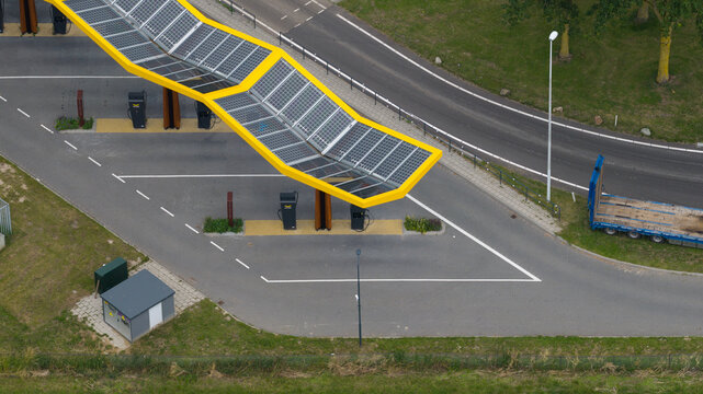 Bunnik, Utrecht, Netherlands - 16 June 2026: Aerial view of a modern electric vehicle charging station with a distinctive yellow solar canopy and charging points.