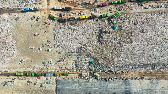Expansive landfill site receives extensive waste collection by numerous garbage trucks under dramatic, dark sky creating an overwhelming mood for environmental management and industrial scale logistic