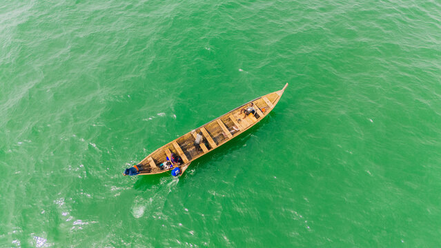 Monrovia, Montserrado, Liberia - 19 June 2026: Aerial view of a wooden fishing boat with fishermen on board navigating the green waters near West Point.
